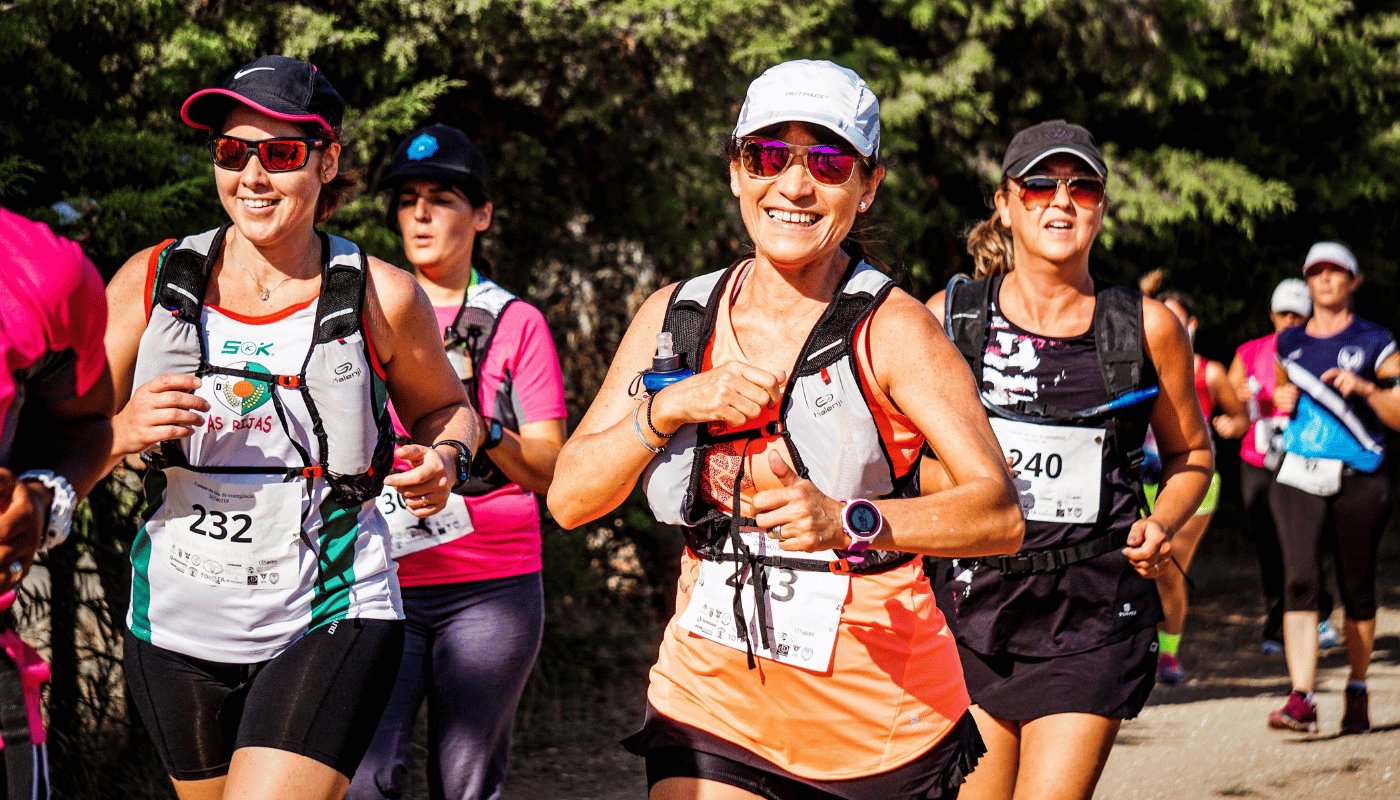 Group of smiling women running a race with hydration packs