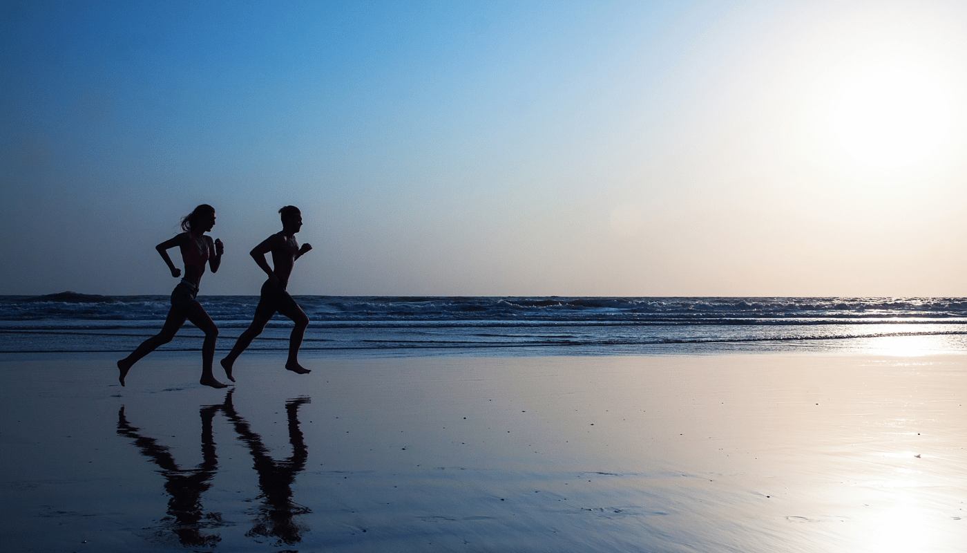 Young man and woman run on a flat beach at sunrise